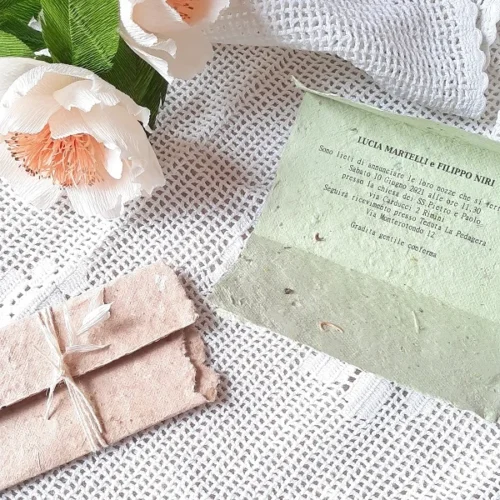 Partecipazione in carta seminabile verde chiaro su tavolino con fiori